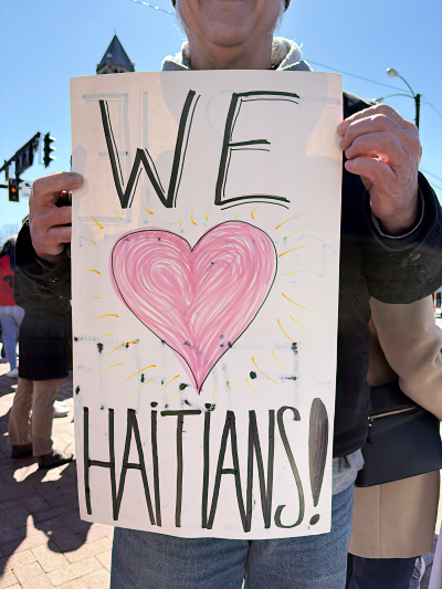 photo of a man holding a sing that reads "We (drawing of a heart) Haitians!"